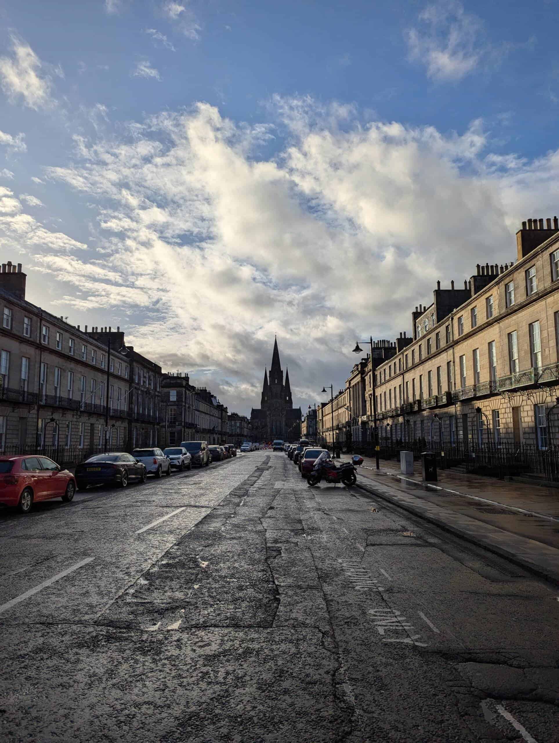 Photo taken in Edinburgh by the author of the piece Vijay Krishnan, featuring a church at the end of a residential street, void of pedestrians, with cars parks either side of the road.