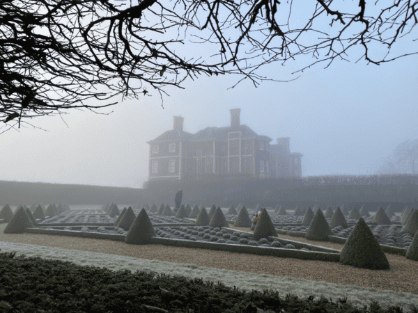 Ham House, photographed through the gardens, which are covered in a dusting of snow on a foggy but blue-sky day